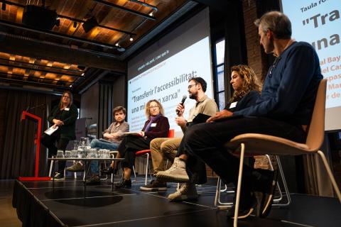 Els cinc ponents de la taula rodona asseguts en butaques baixes. Al costat, Anna Matamala els mira des d'un tamboret alt. Nadal Bayà, al centre de la composició, té el micròfon a la mà.